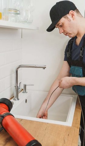 Plumber using drain snake to unclog kitchen sink.