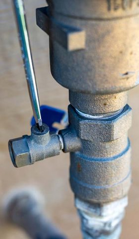 Using a flathead screwdriver to close the test cock next to the vacuum breaker to startup a sprinkler irrigation system in the spring